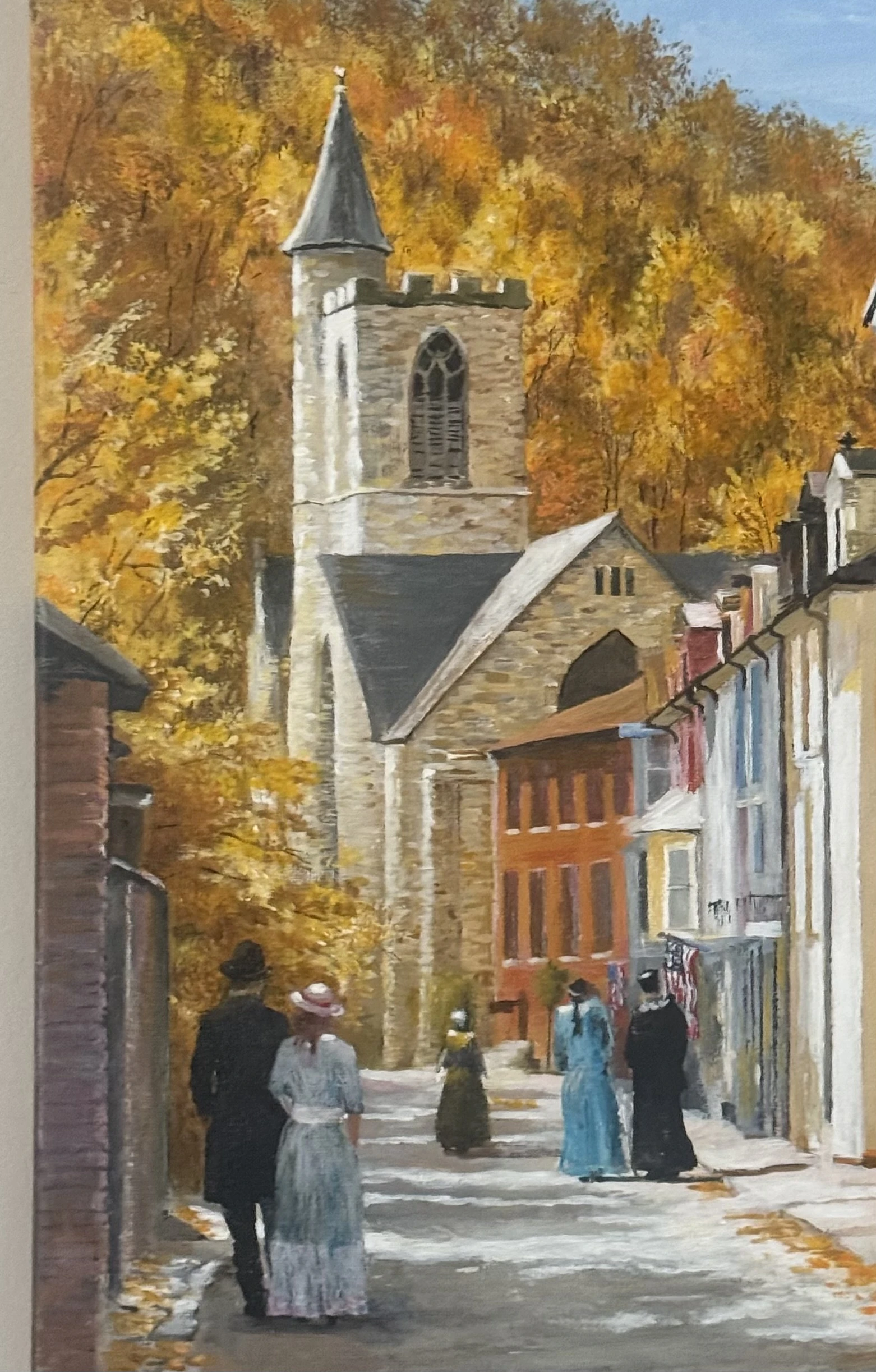 A stone church tower and figures along a village street in autumn