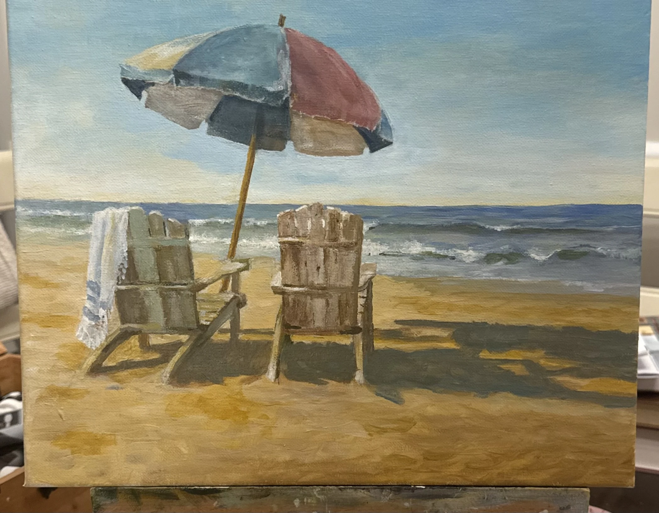 Two wooden beach chairs beneath a striped umbrella facing the ocean